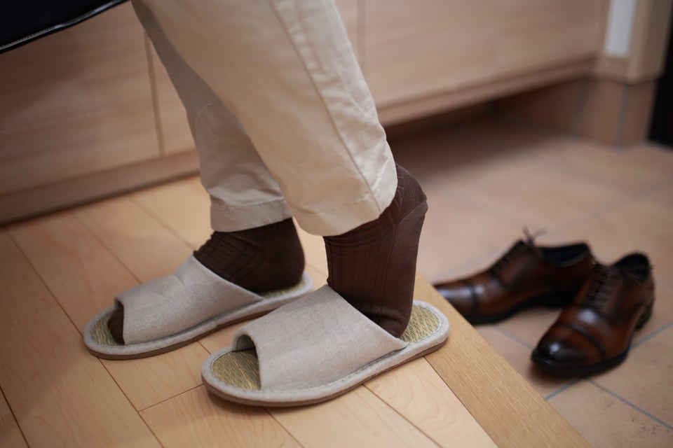 上がり框で靴からスリッパに履き替えている男性