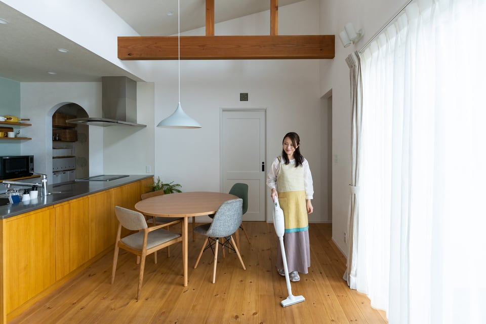 1LDKの間取り内のリビングに掃除機をかける女性