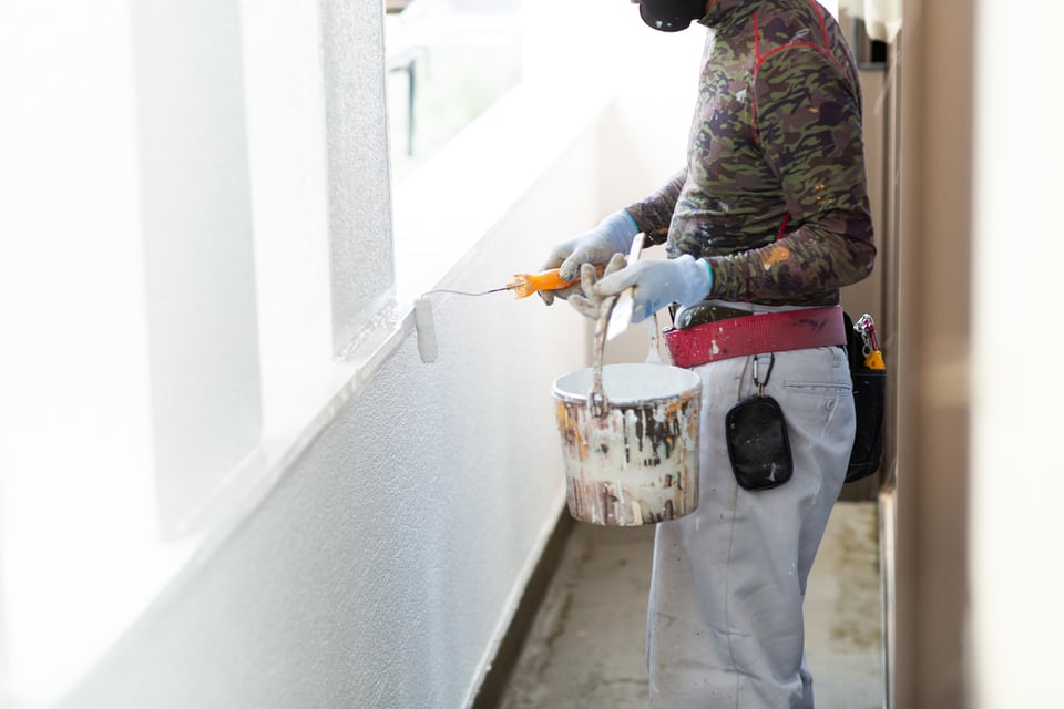 壁に白のウレタン塗料で塗装をしている男性職人