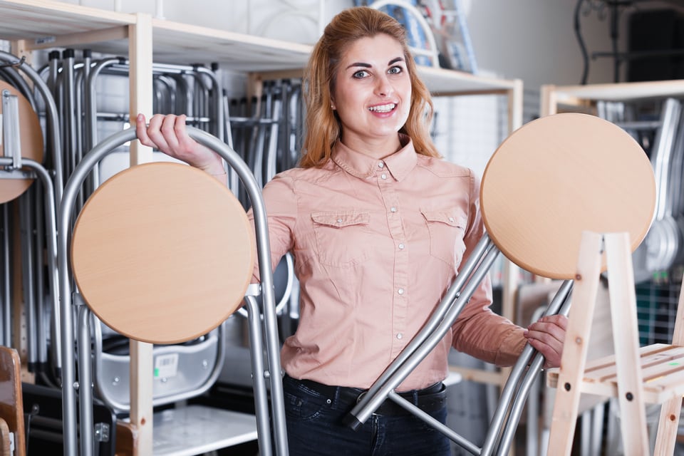 スチールと木製でできた折り畳み型のスツールを説明する販売店員