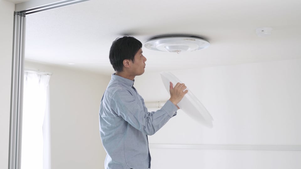 蛍光灯を交換するために照明器具を取り外している男性