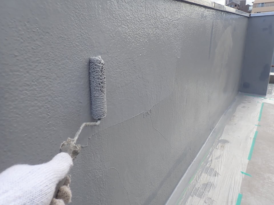 ベランダ外壁にウレタンによる塗膜防水工事を行う作業員