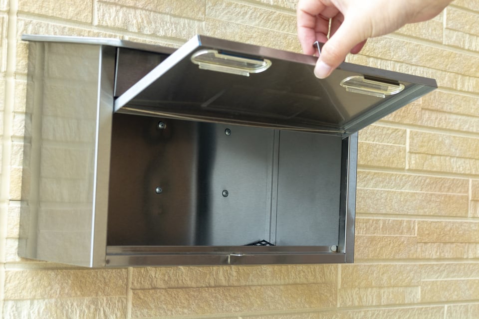 外壁に取り付けられた壁掛け型ポストを開ける人
