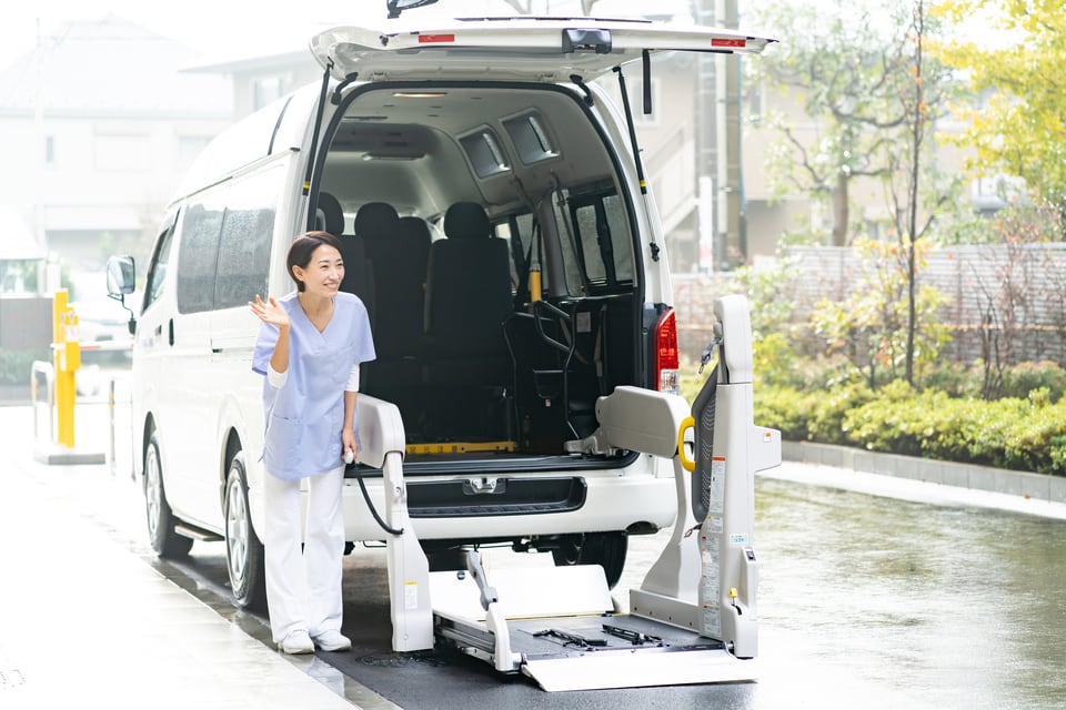ペンダントスイッチで車いすのリフトを下げ挨拶をしているヘルパー