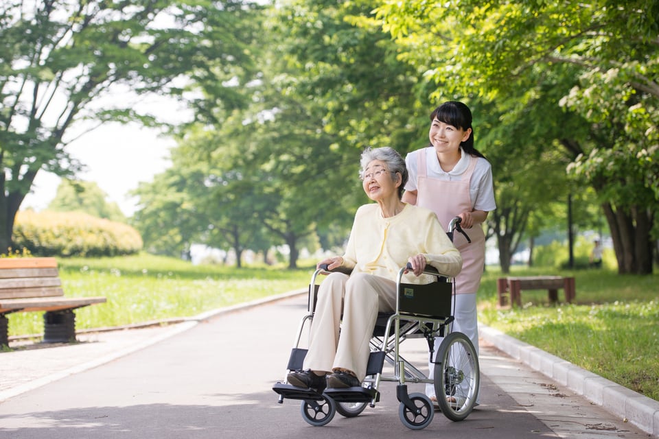 介助用標準型車イスの利用して外出する高齢者と介護スタッフ